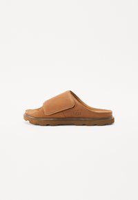 Infradito in pelle marrone con una fascia larga e una soletta testurizzata. Presenta una suola spessa in gomma e il logo UGG sul lato.