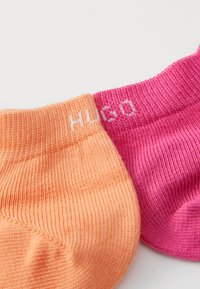 Két pár bokazokni: egy narancssárga és egy élénk rózsaszín, bordázott textúrával és a "HUGO" fehér márkanevével minden mandzsettán.