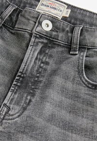 Kitsas sobivusega hallid denim püksid, millel on tuhm finish, metallnupuga kinnitus, vöölõngad ja kaks esipunkti. Tekstureeritud kangas.