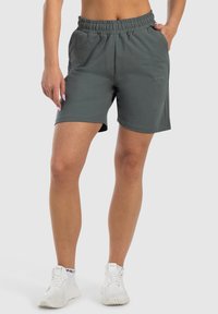 Pantalones cortos grises, hasta la rodilla, hechos de una tela suave, con una cinturilla elástica y bolsillos laterales. Detalle sutil del logo bordado en la parte frontal.