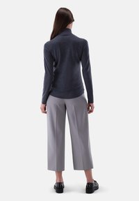 Dunkelgrauer Rollkragenpullover mit einer figurnahen Silhouette, kombiniert mit hellgrauen weiten Hosen und schwarzen Plateauschuhen.