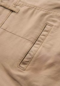 Tissu beige avec une texture lisse, comportant une poche rectangulaire avec des bordures cousues et une fermeture plate.