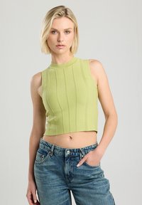 Top corto sin mangas de color verde claro, con una textura acanalada y rayas verticales. Combinado con unos pantalones vaqueros de mezclilla azules, que presentan un ajuste clásico.