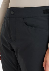 Zwarte buitenbroek met knoopsluiting, zijzakken, een gladde textuur en een klittenbandaccent op de tailleband.