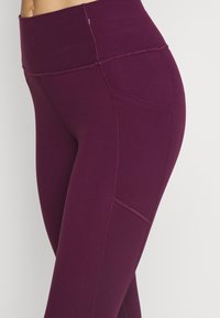 Violetti legginsit korkealla vyötäröllä, joissa on sileä pinta, sivutasku ja näkyvät sauman yksityiskohdat lisäsuunnittelua varten.