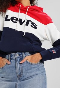 Sweat à capuche avec des sections rouges, blanches et bleu marine, orné d'un grand logo "Levi's". Matière en mélange de coton et poignets côtelés.