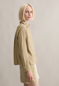 Camicia a quadri verde chiaro con bottoni, collo, maniche lunghe e vestibilità comoda, abbinata a una gonna beige in velluto a coste. Tessuto texturizzato.