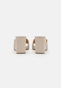 Beige Blockabsatzsandalen mit einer strukturierten Rückseite, offener Zehenpartie und einem subtilen Logoakzent am Absatz, mit einer glatten, polierten Oberfläche.