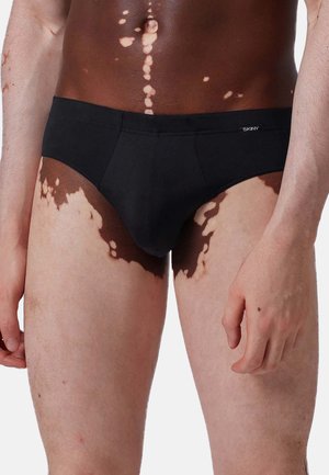 Schwarze Baumwollslips mit einer tiefen Passform, die ein Logo am Bund aufweisen. Glatte Textur und präzise Nähte an den Kanten.