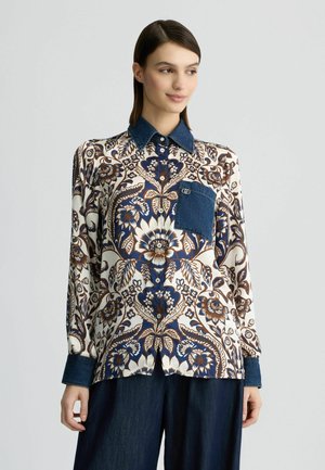 Blusa a maniche lunghe con motivo floreale blu e marrone su fondo crema, con colletto in denim e dettaglio della tasca.
