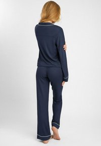 Granatowy zestaw piżamowy składający się z długiego rękawa z kołnierzykiem i białymi lamówkami, w komplecie z dopasowanymi, luźnymi spodniami. Gładka faktura.