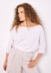 Helles rosa, übergroßes Sweatshirt mit einer kastigen Form, weitem Ausschnitt und 3/4-Ärmeln, kombiniert mit beigen, hoch taillierten Hosen.