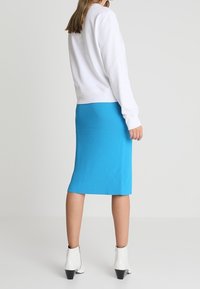 Sweat-shirt blanc avec des poignets côtelés, associé à une jupe côtelée bleu vif et ajustée. Porté avec des bottines blanches à talon noir.