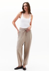 Pantalon beige, texturé, ample avec une taille élastique et un lien de serrage, associé à un débardeur blanc ajusté et des ballerines noires.
