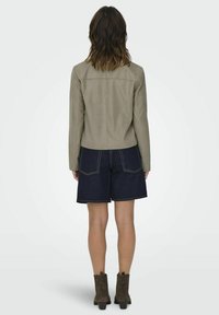 Tan faux suedejacka med långa ärmar, bakstycke-design; bärs över mörka denimshorts med kontrasterande sömmar och två bakfickor.