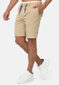 Beige Cordshorts aus Cord mit einem elastischen Bund und schwarzem Kordelzug, mit Seitentaschen und einem Etikett am Saum.