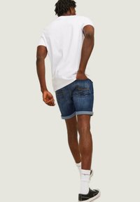 Shorts de denim con dobladillos enrollados, color azul oscuro, bolsillos traseros con detalles de costura. Combinados con una camiseta blanca simple y zapatillas negras.