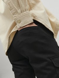 Beige long-sleeve shirt with textured fabric and buttoned cuff, paired with black cargo pants featuring a side pocket and smooth finish.