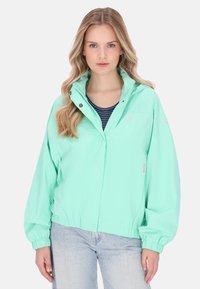 Chaqueta ligera verde menta con cuello alto, puños elásticos, cremallera frontal y bajo redondeado, confeccionada en un tejido suave y resistente al agua.