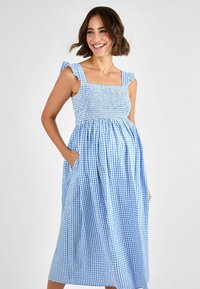 Vestido de cuadros azul y blanco con cuerpo fruncido, tirantes con volantes y bolsillos laterales. Diseño de largo medio con un ajuste relajado.