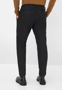 Zwarte broek van gestructureerde stof met zijzakken, achterknopen en dunne enkels, gecombineerd met zwarte schoeisel.