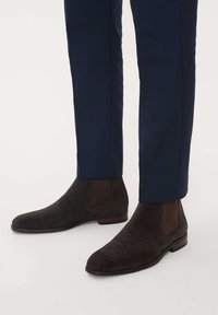 Bruna Chelsea-boots i mocka med elastiska sidopaneler, spetsig tå och låg klack, tillsammans med marinblå skräddarsydda byxor.