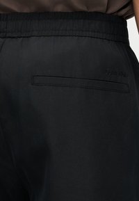 Pantalon noir à taille élastique avec une poche passepoilée à l'arrière et un logo Calvin Klein subtil brodé près de la poche sur le côté droit.