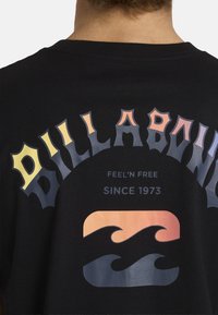 Zwarte katoenen t-shirt met opvallende, veelkleurige "BILLABONG" tekst en golfontwerpen, met een zachte textuur aan de achterkant.