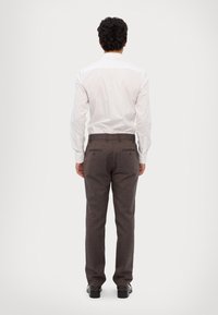 Meeste tagapoolne vaade, kellel on seljas valge pikkade varrukatega särk ja pruunid triibulised püksid, millel on sile tekstuur ja kaks tagumist taskut. Mustad kingad.