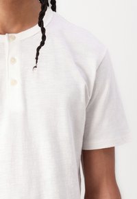 White short-sleeve henley shirt with textured fabric, featuring a round neckline and three front buttons.