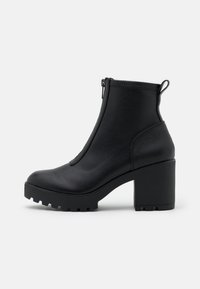 Musta korkokengän nilkkaboots, joka on valmistettu sileästä nahasta, sivuvetoketjukiinnityksellä ja jykevällä teksturoidulla pohjalla. Takana on lenkki, joka helpottaa pukemista.