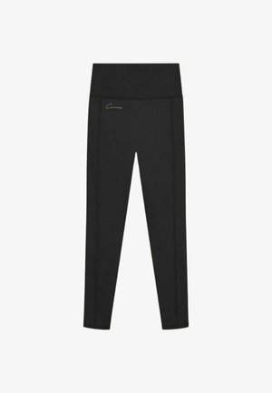 Zwarte, hoge taille, volledig lange leggings met een klein signatuurlogo op het heupgebied tegen een witte achtergrond.