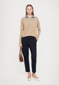 Beige genser med lange ermer over en lyseblå skjorte med krage, kombinert med marineblå bukser og hvite spisse flats; brun skulderveske inkludert.