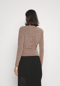 Top a maniche lunghe con design arricciato sul retro, realizzato in un tessuto metallico testurizzato in tonalità terrose, abbinato a una gonna nera plissettata.