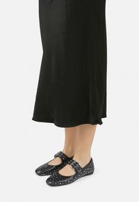 Zapatos de cuero negros con punta cerrada, patrón de lunares y tachuelas plateadas. Presentan una correa con hebilla y una suela plana.
