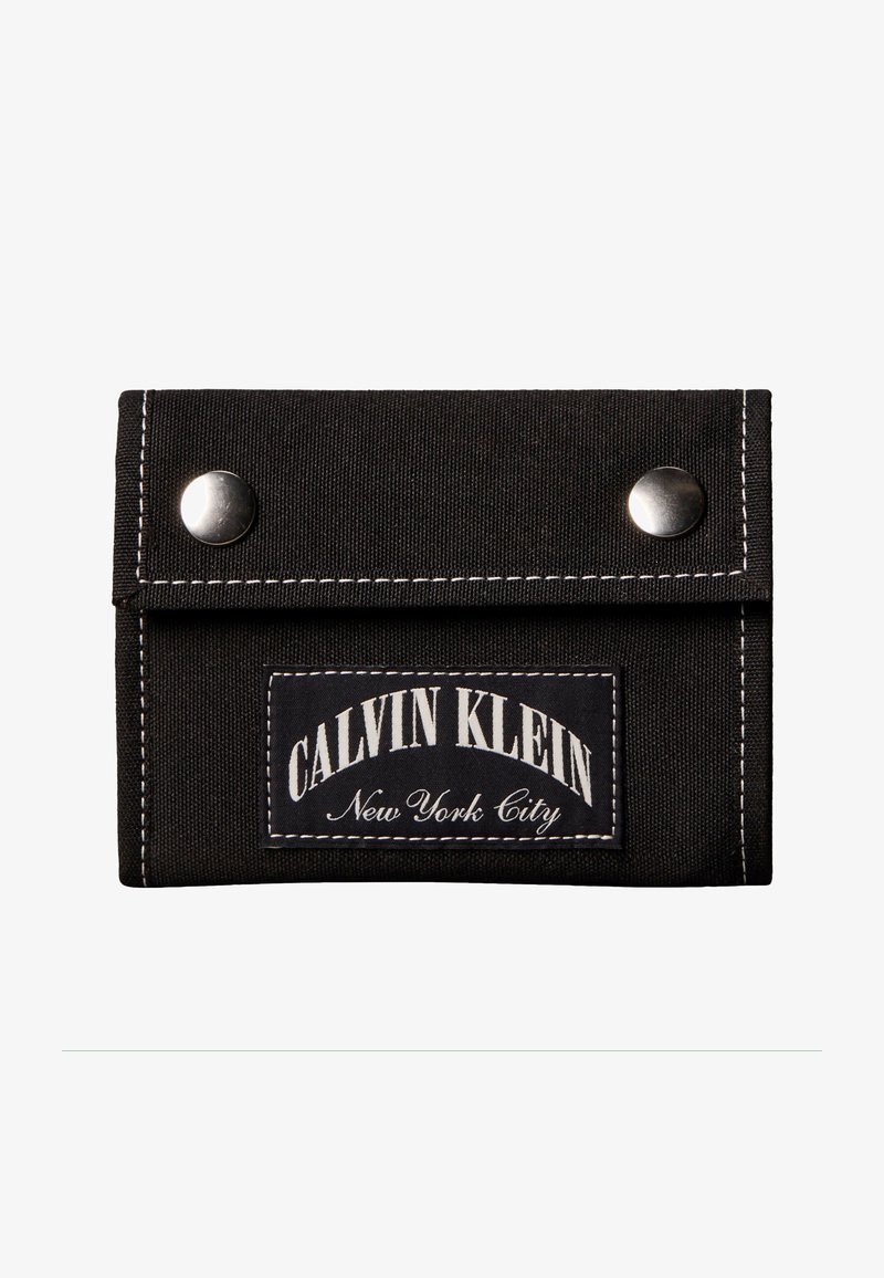 Μαύρο υφασμάτινο πορτοφόλι με δύο ασημένια κουμπώματα και μια ραμμένη ετικέτα στην μπροστινή πλευρά που γράφει «Calvin Klein New York City».