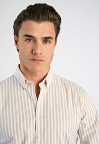 Miesten napillinen paita beige- ja valkoviiruilla, jossa on levitetty kaulus ja pehmeä, sileä puuvillakangas. Viisi näkyvää nappia.