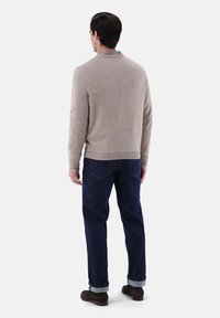 Beiger Strickpullover mit geripptem Kragen, kombiniert mit dunkelblauen Denim-Jeans mit hochgekrempelten Ärmeln und braunen Wildlederschuhen. Minimalistisches Design.