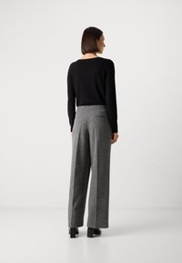 Zwarte longsleeve top gecombineerd met grijze hoge taille wijde broek. De broek heeft een subtiele textuur en een achterzakdetail.