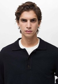 Navy knitted polo shirt with a collar, featuring a two-button placket and ribbed texture. Worn over a white t-shirt.