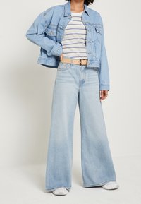 Světle modrá džínová bunda, pruhovaná košile, široké světle modré džíny, béžový opasek a bílé tenisky. Má uvolněný střih a kontrastní švy.