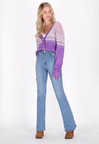 Violet adīta kardigāna ar fair isle rakstu rozā un zilās nokrāsās, kombinēta ar augsto jostasvietu gaiši zilajiem zvana biksēm un brūnām potīšu zābakiem.