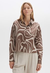 Brown and cream button-up shirt with abstract swirl pattern, lightweight fabric, cropped design, and pointed collar. Paired with light beige trousers.