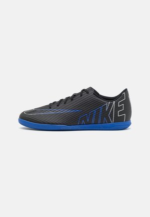 Zapatilla de fútbol sala Nike en negro y azul con cordones, parte superior texturizada y gran texto "NIKE" en el lateral.