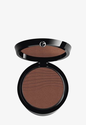 Bronzer mit mattem Finish, untergebracht in einem runden schwarzen Kompakt. Hat eine strukturierte Oberfläche mit Wellenmustern. Der Kompakt öffnet sich mit einem Scharnier.