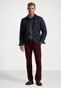 Granatowa pikowana kurtka z brązowym kołnierzem, dwoma kieszeniami na piersi i złotymi guzikami; w połączeniu z bordowymi spodniami i brązowymi mokasynami.