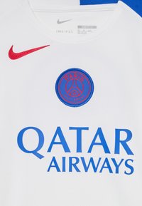 Hvit Nike Dri-FIT-trøye med rød swoosh, blå "QATAR AIRWAYS"-skrift og sirkulært Paris Saint-Germain-logo med blå og røde detaljer.