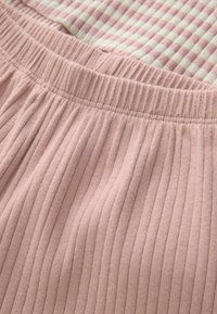 Țesătură ribbed de culoare roz deschis, cu un brâu elastic și o suprapune cu un model de carouri alb și roz vizibil dedesubt.