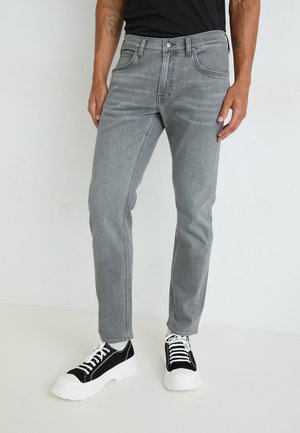 Vaqueros de mezclilla grises con un corte ajustado, diseño de cinco bolsillos y un ligero efecto de desgaste; combinados con zapatillas en blanco y negro con una suela gruesa.