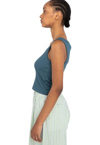 Afskåret tanktop i teal, ribbet tekstur, med ærmeløst design. Kombinationen med stribede høj talje bukser i grøn og hvid.